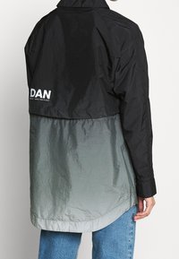 Svart och grå ombre vindjacka med en glänsande yta, med hög krage, långa ärmar och en logotyp på baksidan.