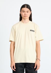 Beige bomulds T-shirt med rund hals og korte ærmer, med 'DICKIES' trykt i sort på venstre brystområde.