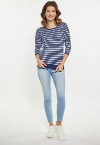 Maglietta a righe blu navy e bianca a maniche lunghe con scollatura rotonda abbinata a jeans skinny azzurri e sneakers bianche. Tessuto morbido, vestibilità casual.