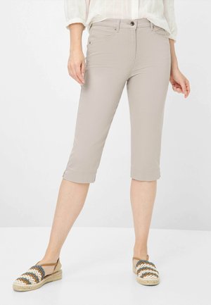 Pantaloni beige a vita alta con taglio slim, chiusura con bottone e orli arrotolati. Il tessuto appare liscio e leggero. Abbinati a espadrillas multicolori.