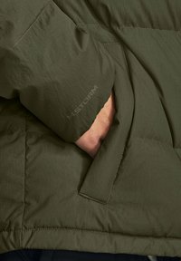 Olijfgroene geïsoleerde jas met een verborgen zijzak en een getextureerde buitenkant met zichtbare stiksels en een "STORM" merkdetail.