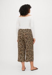 Top bianco a maniche lunghe abbinato a pantaloni cropped con stampa leopardata, caratterizzati da un elastico in vita e un tessuto morbido. Sandali marroni.