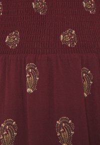 Tissu rouge foncé avec un haut smocké et de petits motifs cachemire olives et beiges dispersés sur le tissu.