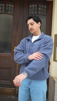 Ung mand i blå fleece, der justerer sin ærme, mens han står foran en trædør med glasfelter.