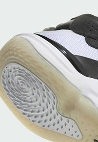 Chaussure de sport avec une tige en mesh blanc texturé, accents noirs et une semelle extérieure en caoutchouc translucide présentant un motif en spirale et des perforations circulaires.