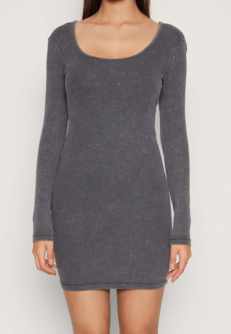 Femme portant une robe mini ajustée, à manches longues, en maille côtelée gris charbon avec un col rond, sur un fond uni.