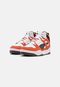 Nilkkapituiset urheilukengät, joissa oranssit ja mustat mokkaiset yksityiskohdat sekä valkoiset nahkapaneelit. Paksut pohjat, joissa musta kumikuviointi.