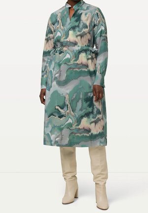Robe midi à manches longues imprimé abstrait vert, gris et beige avec ceinture, portée avec des bottes crème montantes à talons.