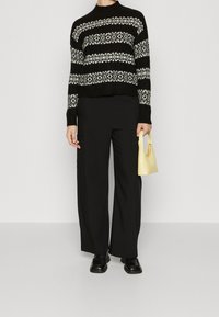 Zwart-wit gestreepte gebreide trui met een cropped ontwerp, gecombineerd met zwarte wijde broek. Houdt een kleine, gestructureerde gele handtas vast.