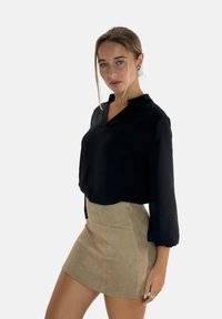 Zwarte blouse met lange mouwen en een diepe V-hals, gecombineerd met een aansluitende, lichtbruine suède minirok. Glad textuur met een ontspannen pasvorm.