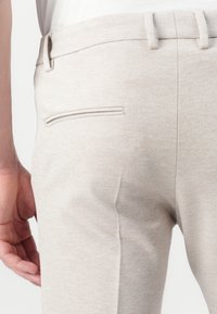 Pantalons beiges clairs fabriqués en tissu texturé, avec une poche arrière simple, une coupe droite et une taille standard.