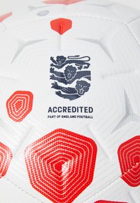Hvid fodbold med røde hexagonale accenter, tekstureret overflade og logo med tre løver, mærket "Akkrediteret, Del af England Fodbold."