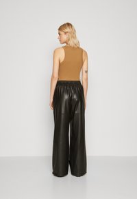 Top de tirantes marrón con un diseño ajustado, combinado con pantalones anchos de cuero negro de cintura alta, que presentan una textura suave y una cinturilla elástica.