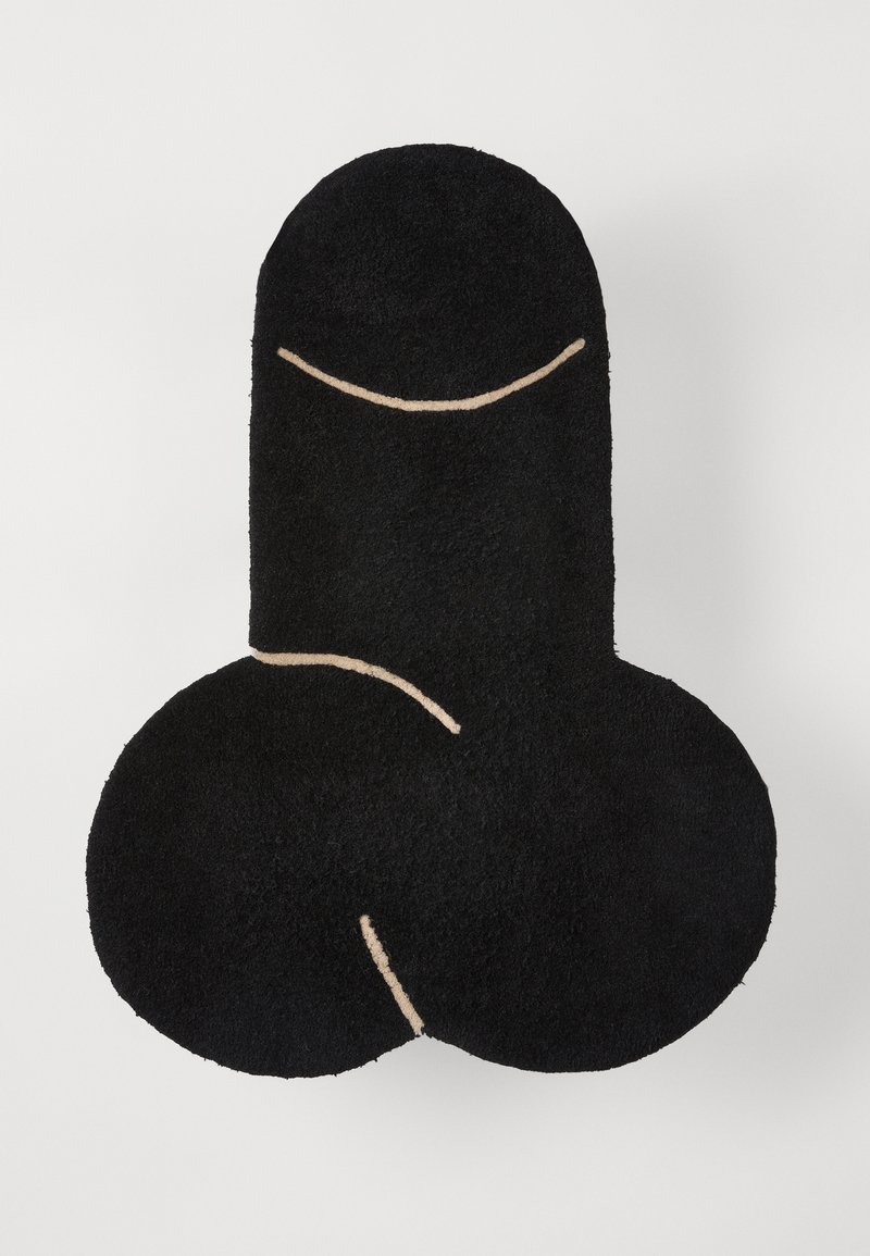 Zwarte harige tapijt in de vorm van mannelijke geslachtsorganen, met beige geborduurde accenten die het ontwerp omlijnen. Zachte textuur en ronde vormen.