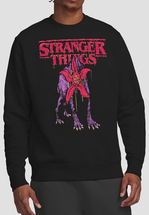 Black sweatshirt with red "Stranger Things" text above a large purple creature with a red flower-shaped face and yellow claws.
