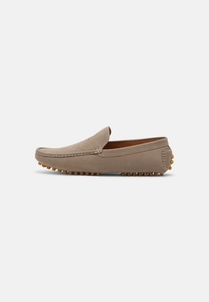 Mocassin beige en daim à enfiler, avec un design de bout mocassin et une semelle en caoutchouc à picots ainsi que des renforts au talon, présenté de profil sur un fond uni.