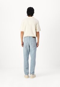 Camisa polo de manga corta en color beige claro y jeans de mezclilla azul claro con un corte relajado, que cuentan con un parche de cuero marrón en la parte posterior de la cinturilla.