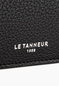 Black leather texture with debossed "LE TANNEUR 1898" logo in silver. Features a smooth surface and fine grain detail.