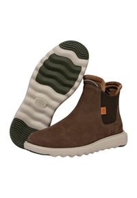 Botines de ante marrón con laterales elásticos, parte superior texturizada y una suela de goma blanca ligera con acentos verdes y un patrón de olas.