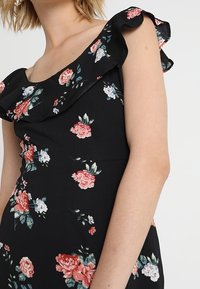 Černé květinové šaty s volány a designem bez ramínek, zdobené růžovými a bílými růžemi, s přiléhavým siluetou a jemnou texturou.