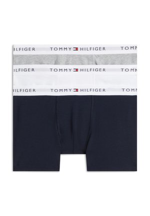 Tre mandlige boxer briefs i grå, hvid og mørkeblå, hver med en hvid linning med Tommy Hilfiger-logo og flag.