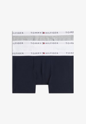 Trois boxers pour hommes en gris, blanc et bleu marine, chacun avec une ceinture blanche arborant le logo et le drapeau Tommy Hilfiger.