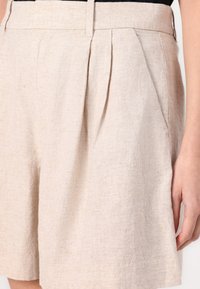 Shorts en lin beige à la texture lisse, dotés de plis avant, d'une taille haute et de poches latérales. Design ajusté avec des lignes épurées.