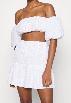Haut court blanc à épaules dénudées avec des manches bouffantes et une jupe mini à volants assortie ; motif floral texturé, taille élastique, tissu léger.
