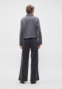 Casaco cinza cropped com gola, combinado com jeans pretos de cintura alta e perna larga. Costuras visíveis e uma textura suave em ambas as peças.