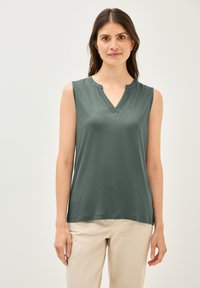 Top verde sin mangas con escote en V y textura suave. Diseño de corte recto, sin patrones visibles, combinado con pantalones de color claro.