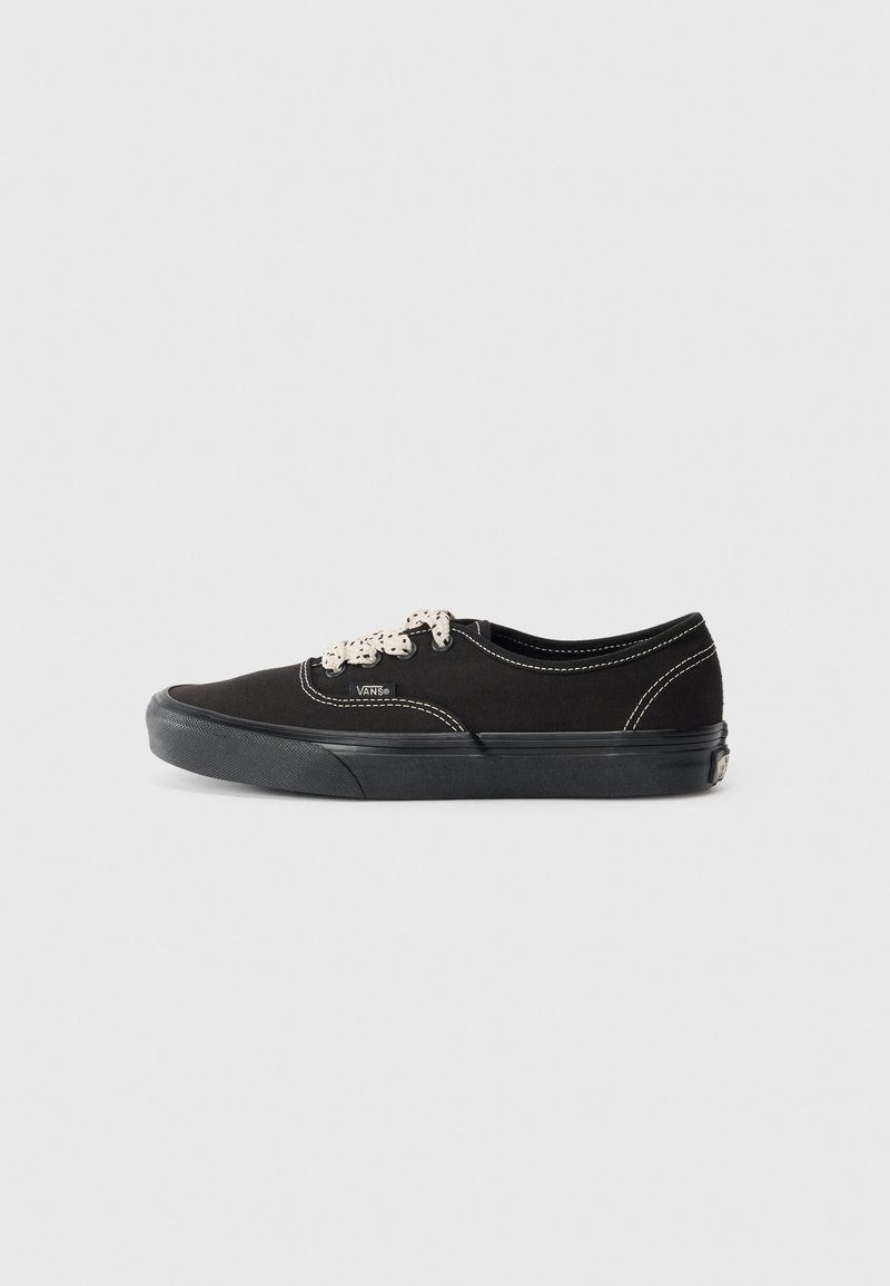 Musta kankaansneaker valkoisilla ompeleilla, pyöreällä kärjellä ja teksturoidulla kumipohjalla. Sisältää mustat nauhat ja logon sivussa.