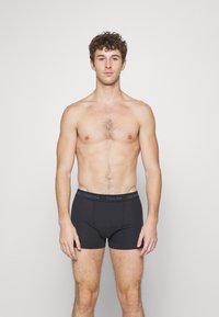 Sorte bomulls trunks med en merket elastisk midjebånd. Stoffet er glatt og elastisk, og gir en tettsittende silhuett.