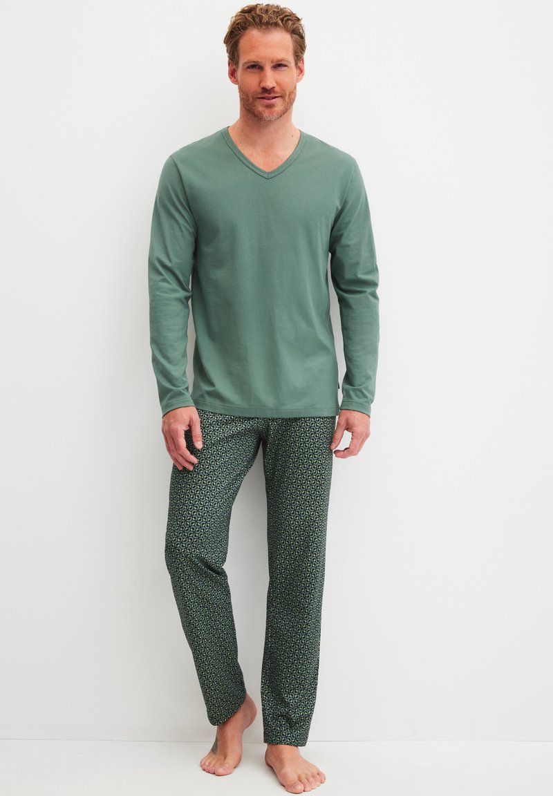 Langsleeve groene V-hals shirt gecombineerd met gestreepte donkergroene broeken met een geometrisch ontwerp. Zachte stof, losse pasvorm.