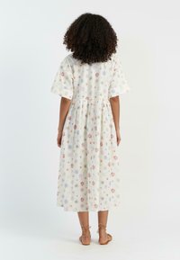 Witte katoenen jurk met kleurrijke bloemen- en sterrenpatronen, korte mouwen, geplooide taille en een lengte tot op de knie. Eenvoudig, ontspannen ontwerp.