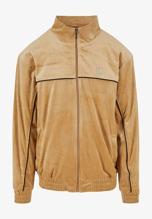 Homok színű zipzáros dzseki puha anyagból. Magas gallérral, fekete részletekkel, valamint rugalmas mandzsettával és alsó résszel rendelkezik. Egyszerű dizájn, minta nélkül.