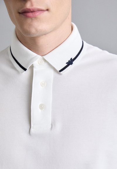 White polo shirt with a textured fabric, featuring a three-button placket and a navy-blue collar accent with a small logo on the left side.