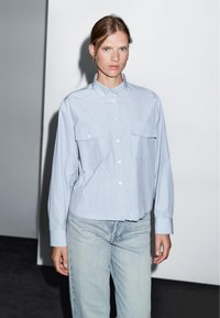 Camicetta a righe blu chiaro con colletto, due taschini sul petto e maniche lunghe, abbinata a jeans dritti blu chiaro.