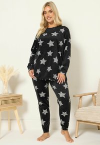 Svart velourpyjamas set med vita stjärnmönster. Topp med lång ärm och avslappnad passform samt matchande tapered byxor. Mjuk textur.