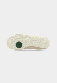 Semelle de sneaker Lacoste en crème avec un motif chevrons texturé, comprenant un accent circulaire vert, en caoutchouc, et des points en relief pour l'adhérence.