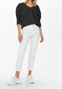 Szary sweter w serek o luźnym kroju, zestawiony z białymi dżinsami o prostym kroju oraz białymi sportowymi butami. Gładka faktura materiału i prosty design.