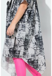 Top sovradimensionato bianco e nero a fantasia con maniche corte, che presenta testi e design astratti, indossato sopra leggings fucsia aderenti.