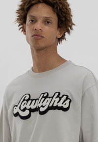 Γκρι φούτερ με υφή, που διαθέτει λευκό και μαύρο κεντημένο λογότυπο "Lowlights" στο στήθος. Στρογγυλή λαιμόκοψη, χαλαρή εφαρμογή.