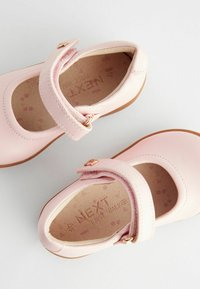 Roza usnjeni čevlji za prve korake s zaobljenim noskom, nastavljivim pasom in mehko roza podlago, ki vsebuje nevsiljiv odtis.