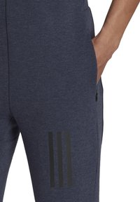 Navyblaue Sweatpants mit einer weichen Textur, ausgestattet mit einer sichtbaren Seitentasche und drei schwarzen vertikalen Streifen am linken Bein.