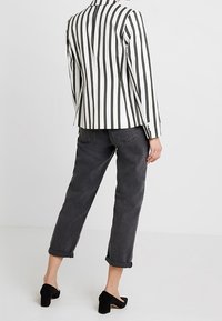 Pruhované sako v černé a bílé barvě, doplněné tmavě šedými zkrácenými džínami. Celkový vzhled dotvářejí černé boty na blokovém podpatku. Čistý, moderní design.