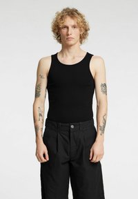 Czarny prążkowany top na szerokich ramiączkach, o dopasowanym kroju i gładkiej fakturze, w zestawieniu z luźnymi czarnymi spodniami zapinanymi na guzik.