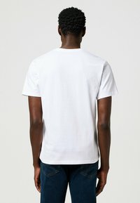 Camiseta blanca de manga corta con cuello redondo, textura de algodón suave y corte regular, combinada con jeans de denim azul oscuro.