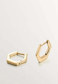 Pendientes hexagonales de oro con textura suave y acabado pulido. Cuentan con una bisagra para el cierre y bordes geométricos afilados.