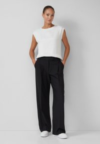 Un haut sans manches blanc, avec une texture en crêpe, associé à un pantalon noir à jambes larges, en tissu lisse avec un léger éclat, complété par des baskets blanches.