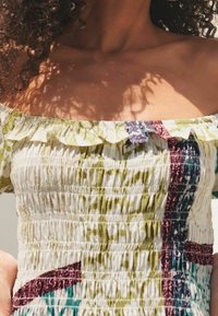 Top bustier à épaules dénudées avec un design smocké en blanc, vert et bordeaux, avec des bords à volants et un tissu à motif coloré.